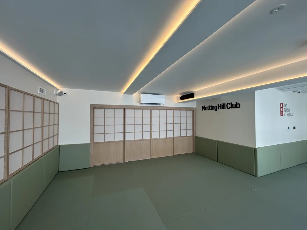 Sage green dojo with sliding door storage, white ceiling with linear lighting stripes, creating a clean and organized training space.