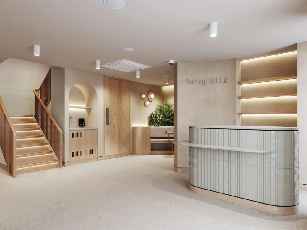 Reception area with cream tones, a wooden staircase, and a tiled reception desk featuring the Notting Hill Club logo.